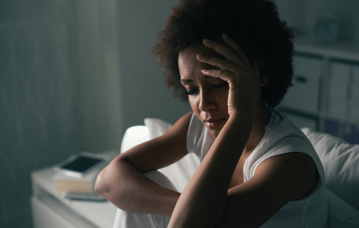 A woman looks down with her hand on her head.