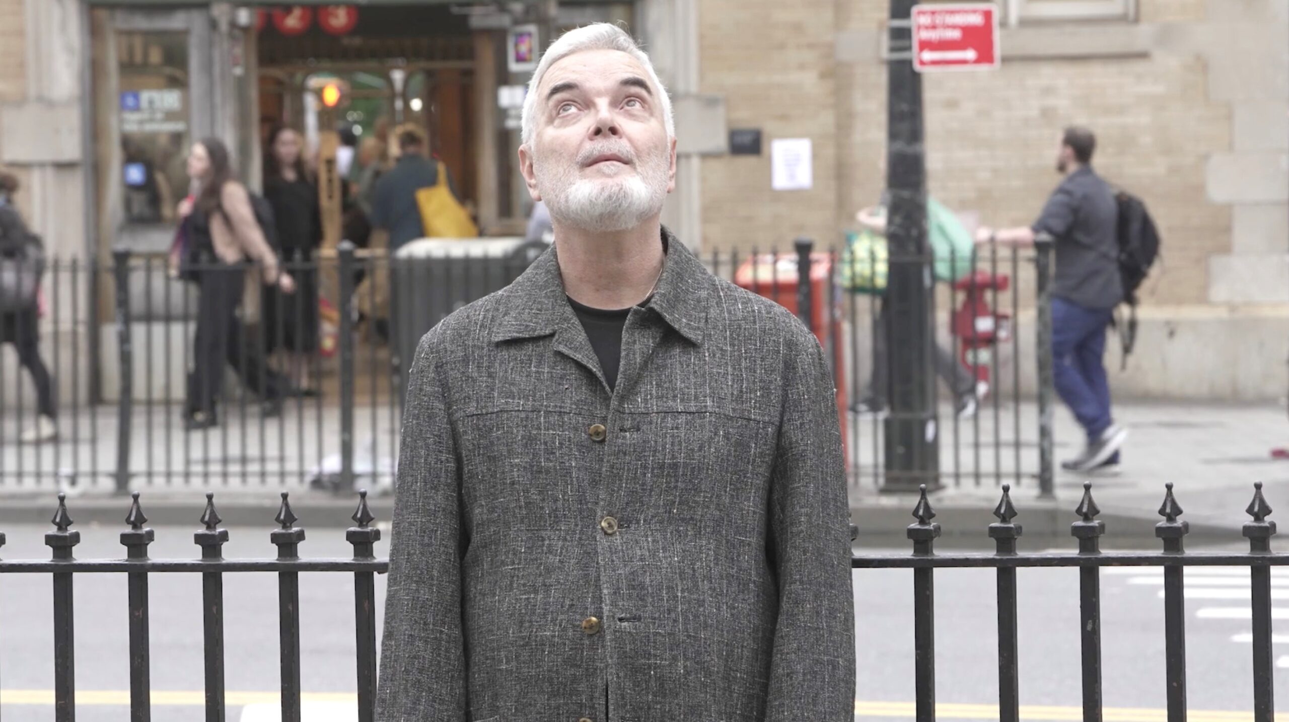 Photo of Mel Odom standing on a street sidewalk in NYC, gazing up at the sky.