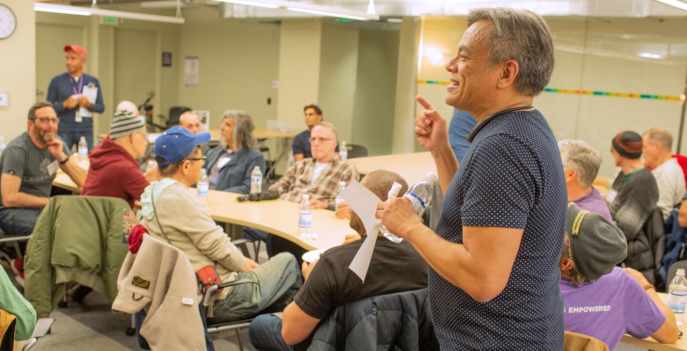 Vince Crisostomo stands at front of room speaking to a group of seniors. He is smiling and looks engaged.