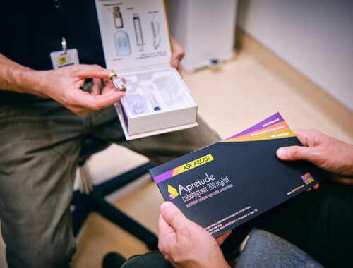 A Strut staff member hands an Apretude injectable PrEP brochure to a seated person in the Magnet clinic.