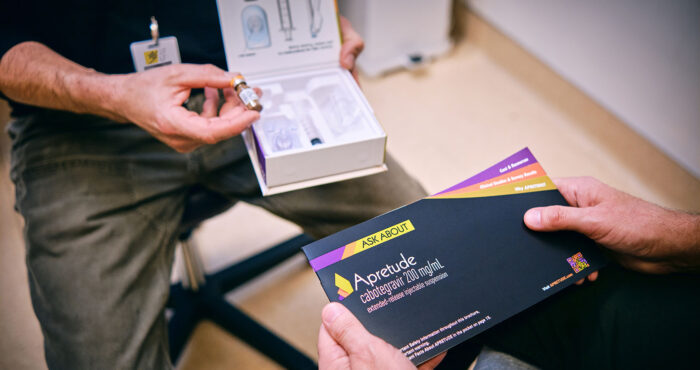 A Strut staff member hands an Apretude injectable PrEP brochure to a seated person in the Magnet clinic.